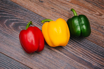 Sweet pepper multicolored on a dark wooden background. Red, yellow and green peppers are on the table. Bright vegetable