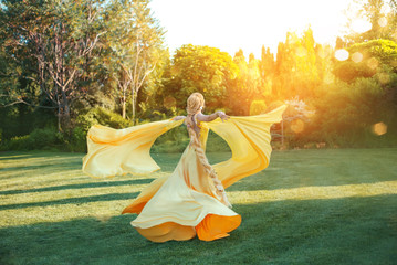 bright divine sun light. Art Fantasy happy woman dancing spinning hand raised yellow silk dress,...