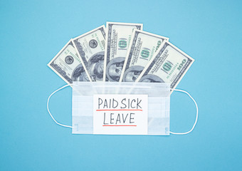 Medical mask with dollars and the words paid sick leave on a blue background. Concept of economic dependence on the COVID-19 coronavirus pandemic