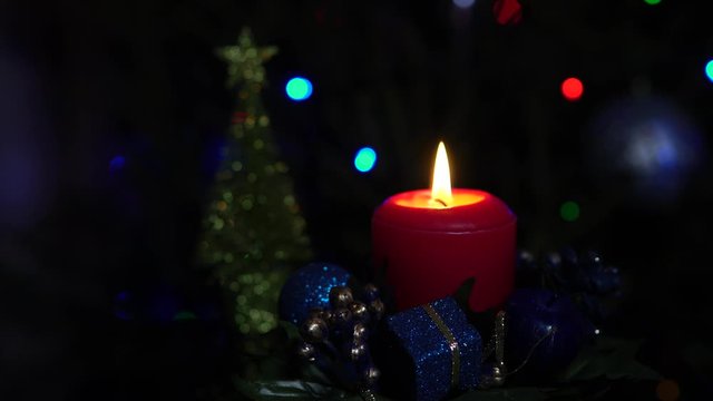 The end of the Christmas holidays. Extinct red candle in a candlestick and Christmas tree decoration. Behind a flashing garland on a spruce