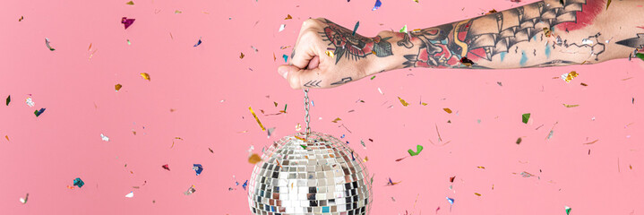 Tattooed hand holding a Christmas disco ball and confetti in the air