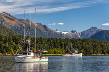 Fishing boat sailing in harbor and another fishing boat drifting behind it. Mountains, forest and...