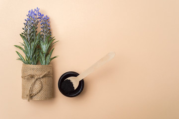 Flowers, activated charcoal and wooden spoon on camel color background. Zero waste concept.