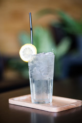 Lemonade with ice in fancy glass with straw, there are lemons and a half on glass.