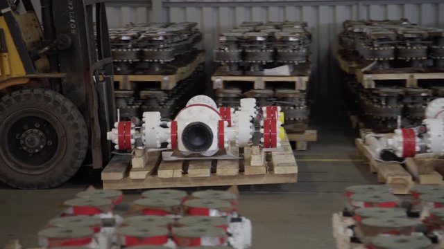 Man on forklift transporting Oil and Gas Wellhead tree equipment production plant on pallets in warehouse. Modern tendencies of machine engineering. Equipment for wellhead conncetion of oil gas wells.