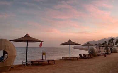 Beach furniture in front of a pink sunset by the ocean in South Sinai, Egypt