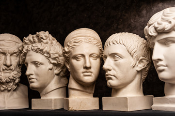 Group gypsum busts of ancient statues human heads for artists on a dark background. Plaster...