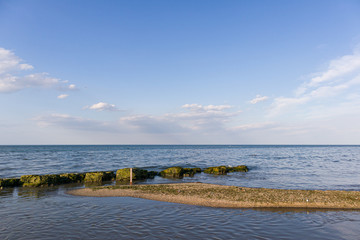 A small sand band leading to a natural breakwater. With blue, clean sky and clouds on background.