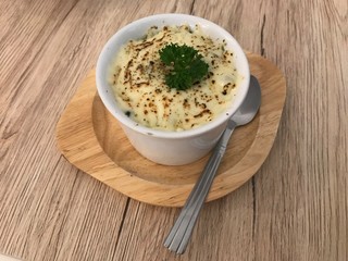 Homemade baked spinach with cheese in white bowl white on wooden table.