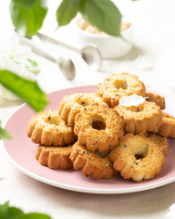 Shortbread in a pink ceramic plate on a light table. A plate of cookies on the table among the flowering trees. The plate is full of cookies. Rustic homemade cakes. Tea party with pastries