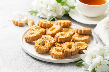 Shortbread in a pink ceramic plate on a light table. A plate of cookies on the table among the flowering trees. The plate is full of cookies. Rustic homemade cakes. Tea party with pastries