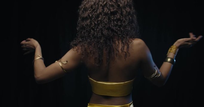 View from the back on a young woman belly dancing, curly hair, 4k