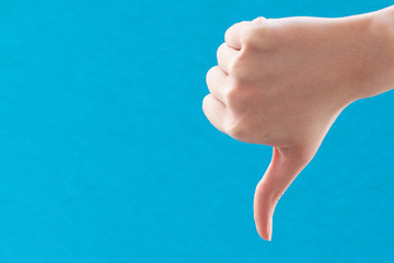 Close-up of female hand holding thumb down sign with hand on blue background. Negative hand gesture, denial