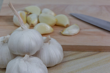 A pile of fresh garlic with a background of peeled garlic pieces on a wood cutting board and knife.