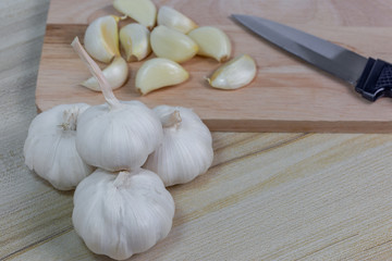 top view with a pile of fresh garlic on the wood floor and a piece of garlic with a knife