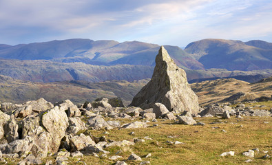 Large rock formations on the summit of Grey Friar with distant views of Fairfield, Seat Sandle, Dollywaggon, and Helvellyn on a sunny day in the Lake District.