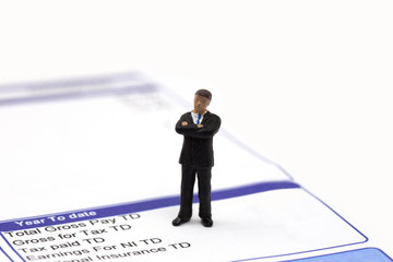 Miniature scale model businessman standing on a wage pay slip showing earnings deductions.  Isolated on a white background