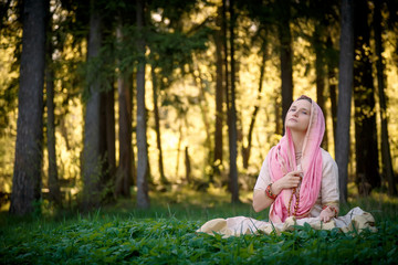 Woman in Indian clothes sitting in sunny green forest meditating
