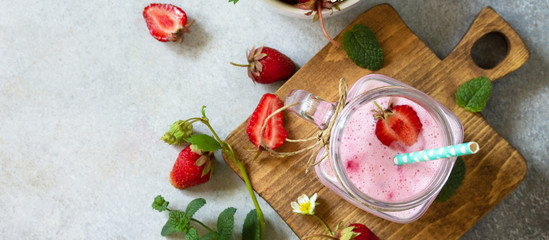 Natural detox, fruit dessert, healthy dieting concept. Strawberry fruit Yogurt smoothie or milk shake in glass jar on a light stone or slate table. Top view flat lay background. Banner.