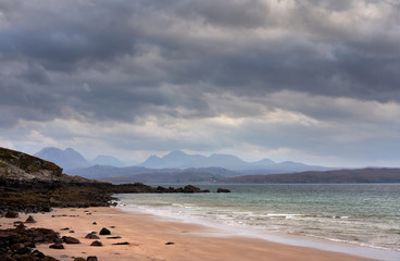 Rays of autumn sunlight breaking through the cloud at the beach of Big Sand near Gairloch with distand views of the torridon mountains in the Scottish Highlands, Scotland, UK.