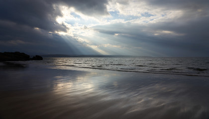 Obraz premium Rays of autumn sunlight breaking through the cloud aover the wet beach of Big Sand near Gairloch in the Scottish Highlands, Scotland, UK.