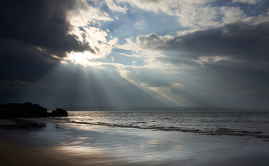 Rays of autumn sunlight breaking through the cloud on the wet and rocky beach of Big Sand near Gairloch in the Scottish Highlands, Scotland, UK.