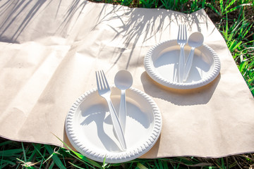 Fototapeta na wymiar outdoor picnic with biodegradable cornstarch cookware on craft paper. shadow from the grass. place for text. eco friendly. spoon, fork, plate of environmentally friendly materials. 