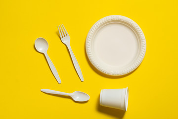 disposable biodegradable fork, spoon, glass and plate of corn starch on a yellow background. environmentally friendly dishes. isolate. place for text. modern ecoplastics replacement