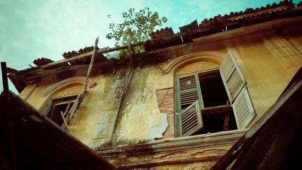 Fototapeta na wymiar Orange wall with green broken window with crooked roof