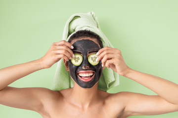 Obraz na płótnie Canvas Happy smiling girl applying facial carbon mask portrait - Young woman having skin care cleanser spa day - Healthy beauty clean treatment and and self care lifestyle concept - Green background