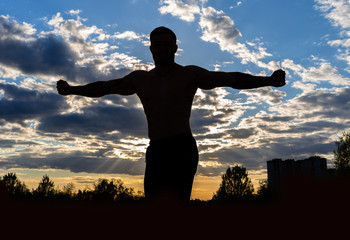 Silhouette of a strong muscular man on a background of sunset sky. Fitness in the evening on the street.