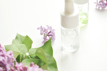 Cosmetic oil in a bottle with a pipette on a background of flowers and a white table.