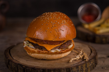 Hamburger with french fries, ketchup, mustard and fresh vegetables on a cutting wooden board.