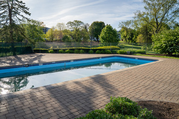 Swimming pool with concrete pavers just after opening for the season with green water and debris