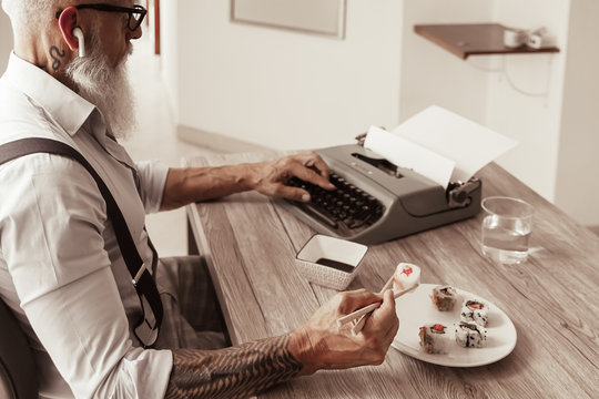 Man enjoying eating fresh colorful asian sushi using chopsticks. This man writing with the old typewriter in the office. Image