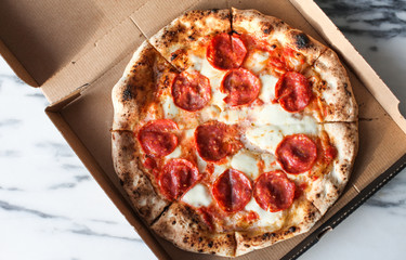 Top view of a fresh Italian pepperoni pizza in a paper box on marble table background