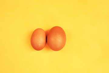 Brown eggs on yellow background. Size difference concept between two farm eggs.