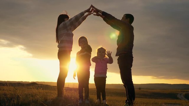 Silhouette of a happy family with young children dreaming of their own home. Parents hold their hands over their children's heads, a symbol of home, home, and child protection.