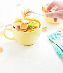 Mini pancake cereal in light green mug, white concrete background ready to serve on breakfast. New food trend. Copy space for text. Butter and mint leaves, milk, checkered aqua cloth. Hand with fork