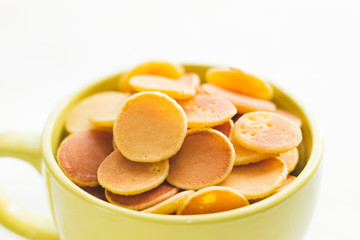 Mini pancake cereal in light green mug on white concrete background ready to serve on breakfast. New food trend during covid-19 lockdown. Copy space for text. Macro close up shoot