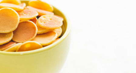 Mini pancake cereal in light green mug on white concrete background ready to serve on breakfast. New food trend during covid-19 lockdown. Copy space for text. Macro close up shoot