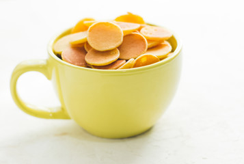 Mini pancake cereal in light green mug on white concrete background ready to serve on breakfast. New food trend during covid-19 lockdown. Copy space for text. Macro close up shoot