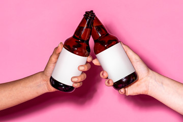 Hands holding beer bottles against a pink background