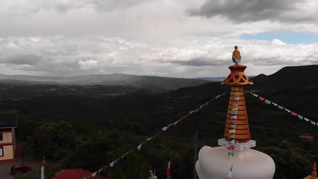 Orbital view of the main stupa of the Tibetan Buddhist temple of Dag Shang Kagyu, going around the prayer flags and admiring the beauty of the background mountains with a cloudy sky