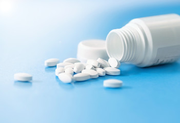 Pills spilled out of white bottle on light blue background with copy space. Medical healthcare concept