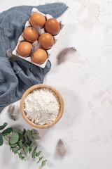 Obraz na płótnie Canvas Cooking and baking concept. Baking ingredients on white background. Eggs and flour. Home baking, homemade cooking flat lay top view