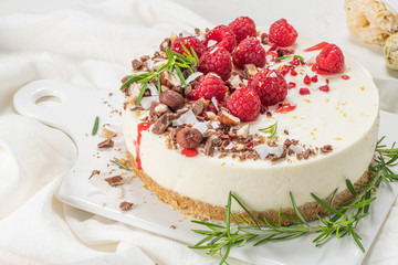 Cheesecake with raspberries, chocolate, hazelnuts and rosemary leaves on kitchen coutertop
