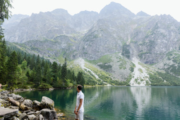 The man standing and watching a quiet lake in the mountains
