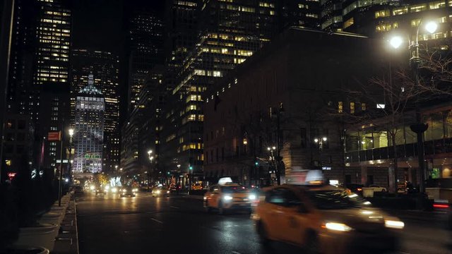 yellow taxis that travel in the night in an avenue that crosses 53th street in New York, surrounded by skyscrapers with illuminated windows, the lights of the traffic lights are green