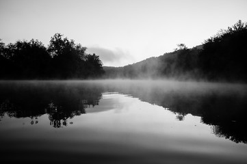 Fog rises from the calm water on a cool summer morning.